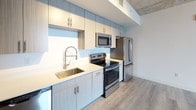 Located at 35 SW 6th Street in Miami's vibrant Brickell neighborhood, this contemporary unit blends industrial design with modern finishes throughout. The open-plan living area is defined by an exposed concrete ceiling and striking navy accent walls that create a bold, urban aesthetic. Light gray hardwood-style flooring runs seamlessly across the space, complementing the neutral palette and enhancing the airy feel.

Floor-to-ceiling windows in the living area and bedroom frame sweeping panoramic views of the Miami skyline, flooding the interior with abundant natural light. A sliding glass door provides direct access to the outdoors, further connecting the space to its urban surroundings.

The kitchen is thoughtfully designed with light wood cabinetry extending to the ceiling, white quartz countertops, a stainless steel under-mount sink with a professional-style pull-down faucet, and a full suite of stainless steel appliances including a range, microwave, dishwasher, and refrigerator. A louvered utility closet adds practical storage nearby.

The bedroom features its own exposed concrete ceiling, a large closet with bi-fold doors, and the same expansive city views. Two full bathrooms are finished with large-format neutral tile surrounding the tub-shower combinations, wood-look flooring, and modern vanities with white countertops.