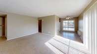 This single-floor unit offers a practical and comfortable layout across several well-defined spaces. The kitchen is outfitted with warm oak cabinetry providing ample upper and lower storage, light-toned laminate countertops forming an L-shaped work surface, a double stainless steel sink, a white electric range with overhead ventilation, and a full-size refrigerator. Tile flooring and a window fitted with horizontal blinds add functionality and natural light to the space.

The living area is generously sized, featuring neutral-toned carpet, a textured ceiling, and a ceiling fan with light fixture. A large sliding glass door dressed with vertical blinds floods the room with natural light and offers outdoor views, creating a bright and open atmosphere.

The bedrooms continue the carpeted flooring and neutral wall tones, each equipped with windows featuring vertical blinds and baseboard heating units. One bedroom includes access to closet space. The bathroom is finished with tile flooring, a full-size soaking tub with overhead shower, white tile surround, a window for natural light, and a vanity with integrated sink. Throughout, the unit maintains a consistent, understated aesthetic with textured ceilings and clean white trim.