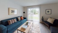 This two-floor residence offers a thoughtfully designed layout with a clean, modern aesthetic throughout. The living room serves as a welcoming central space, featuring wood-look flooring, a textured ceiling, and a large sliding glass door dressed with vertical blinds that floods the room with natural light and opens to a view of the surrounding greenery outdoors. Adjacent to the living area is a cozy dining nook with a ceiling fan, baseboard heating, and room for a round dining table — ideal for everyday meals. The galley-style kitchen is well-equipped with light wood cabinetry, crisp white countertops, stainless steel appliances including a dishwasher, range, and refrigerator, complemented by wood-look tile flooring. Multiple bedrooms are spread across both floors, each finished with plush carpet, ceiling fans, and ample natural light from well-placed windows offering views of lush outdoor foliage. Several bedrooms include sliding closets for convenient storage. The bathroom features warm wood-tone cabinetry, a full soaking tub with shower, and durable wood-look plank flooring, creating a clean and functional space. Throughout the home, a neutral color palette and consistent finishes lend a cohesive, contemporary feel.