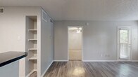 Located at 2707 Frankford Rd in Dallas, TX, this one-bedroom, one-bathroom unit offers a well-organized single-floor layout designed to maximize functionality. The open living room is a standout space, featuring durable wood-look luxury vinyl plank flooring, a classic white-surround wood-burning fireplace, and multiple windows with blinds that invite an abundance of natural light, creating a bright and welcoming atmosphere. The kitchen is efficiently designed with white cabinetry, dark granite-style countertops, a tile mosaic backsplash, and black appliances including a range, microwave, and refrigerator. A peninsula counter provides additional prep space and a convenient breakfast bar. Built-in open shelving adds practical storage to the kitchen area. The bedroom is a comfortable, well-lit retreat with soft wall-to-wall carpeting, a ceiling fan with light fixture, and a generously sized window overlooking the outdoors. A dedicated closet provides ample storage. The bathroom features white cabinetry, a dark countertop vanity with a wide mirror, and a tiled shower-tub combination. Textured ceilings are present throughout, and the neutral gray color palette gives the entire unit a clean, cohesive aesthetic.