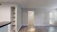 Located at 2707 Frankford Rd in Dallas, TX, this one-bedroom, one-bathroom unit offers a well-organized single-floor layout designed to maximize functionality. The open living room is a standout space, featuring durable wood-look luxury vinyl plank flooring, a classic white-surround wood-burning fireplace, and multiple windows with blinds that invite an abundance of natural light, creating a bright and welcoming atmosphere. The kitchen is efficiently designed with white cabinetry, dark granite-style countertops, a tile mosaic backsplash, and black appliances including a range, microwave, and refrigerator. A peninsula counter provides additional prep space and a convenient breakfast bar. Built-in open shelving adds practical storage to the kitchen area. The bedroom is a comfortable, well-lit retreat with soft wall-to-wall carpeting, a ceiling fan with light fixture, and a generously sized window overlooking the outdoors. A dedicated closet provides ample storage. The bathroom features white cabinetry, a dark countertop vanity with a wide mirror, and a tiled shower-tub combination. Textured ceilings are present throughout, and the neutral gray color palette gives the entire unit a clean, cohesive aesthetic.
