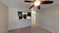 This single-floor unit offers a functional and comfortable layout designed for everyday living. The living area is anchored by a ceiling fan with a light fixture and features soft wall-to-wall carpeting throughout, creating a warm and inviting atmosphere. A textured ceiling adds a classic touch to the space. Natural light filters in through blinded windows, brightening the interior. A cozy fireplace is situated in the main living area near the front entry door, providing a welcoming focal point.

The kitchen is accessed via a pass-through counter with light stone-toned countertops, offering a convenient connection to the living space. Dark espresso cabinetry lines the kitchen walls, complemented by black appliances including a refrigerator and oven range. Wood-look flooring runs throughout the kitchen, providing a clean contrast to the carpeted areas.

The bedrooms are generously proportioned, each equipped with ceiling fans, plush carpeting, and windows with blinds that allow for natural light and privacy. One bedroom provides direct access to an outdoor area through a glass door.

The bathroom is well-appointed with dark wood cabinetry, a single vanity featuring a light speckled countertop, a large mirror, and a full-size soaking tub and shower combination. Wood-look flooring completes the bathroom's clean and cohesive aesthetic.