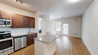 Located at 55 Dorset Crossing Dr in Simsbury, Connecticut, this efficiently designed single-floor unit offers a thoughtfully arranged layout that maximizes every square foot. The open-concept living and kitchen area flows seamlessly, anchored by warm hardwood-style flooring that extends throughout the main living space. Large windows fitted with blinds invite generous natural light, creating a bright and airy atmosphere, while a private exterior door leads to an outdoor area with views of surrounding greenery.

The kitchen is a standout feature, boasting rich dark-stained cabinetry with sleek hardware, granite countertops, a subway tile backsplash, and a full suite of stainless steel appliances including a refrigerator, range, microwave, and dishwasher. A peninsula with matching granite provides additional counter space and serves as a natural divider between the kitchen and the living area.

The bathroom is clean and well-appointed, featuring a white vanity with under-sink storage, a large mirror, and durable stone-look tile flooring that adds a classic touch. The neutral, light-toned walls throughout the unit create a versatile canvas adaptable to a variety of interior styles. This unit combines functional design with modern finishes for comfortable, low-maintenance living in Simsbury.