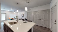 This well-designed single-floor residence offers a thoughtful layout that seamlessly blends style and functionality. The open-concept kitchen is a standout feature, showcasing rich dark cabinetry, stainless steel appliances, a grey tile backsplash, and a large white quartz island with an undermount sink and seating for multiple guests. Pendant lighting overhead adds a modern touch, while wood-look flooring ties the space together. The kitchen flows naturally into a bright living area, complete with a ceiling fan, a dedicated workspace nook, and access to ample closet storage behind a set of paneled double doors. The bedroom is a comfortable retreat, featuring plush carpet, natural light from two windows, and a ceiling fan. It connects to a generously sized walk-in closet outfitted with multiple hanging rods and shelving, providing exceptional storage capacity. The en-suite bathroom is finished with light wood-look flooring, a dark-toned vanity with ample counter space, open shelving, and a glass-enclosed walk-in shower clad in large-format tile. Throughout the residence, a neutral color palette, clean lines, and modern finishes create a cohesive and inviting ambiance.