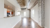 Located at 1237 Harmony Lake Dr in Cottleville, MO, this 1-bedroom, 1-bathroom unit showcases a bold industrial-modern design throughout. Polished concrete floors run seamlessly across the entire space, reflecting natural light that pours in through multiple large windows fitted with clean white blinds. The open-concept living and kitchen area is anchored by soaring ceilings with exposed concrete columns, visible ductwork, and ceiling-mounted fans, creating a loft-like atmosphere with generous vertical volume.

The kitchen is well-appointed with warm wood cabinetry, granite-look countertops, black appliances including a refrigerator, range, microwave, and dishwasher, plus track lighting overhead. A dedicated pantry provides additional storage just off the kitchen. The granite-topped breakfast bar separates the kitchen from the expansive living area, which offers abundant space and multiple windows with outdoor views.

The bedroom is generously sized, featuring the same polished concrete flooring, exposed concrete columns, and soaring ceilings that carry the industrial aesthetic throughout. A walk-in closet with wire shelving offers practical storage. The bathroom includes a glass-enclosed shower and toilet compartment finished in stone-look tile, providing a clean and functional design. The overall ambiance is open, airy, and distinctly contemporary.