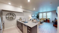 This single-floor residence offers a thoughtfully designed open-concept layout that seamlessly connects the kitchen, dining, and living areas. The kitchen serves as the heart of the home, anchored by a granite-topped island with an undermount sink, stainless steel appliances including a refrigerator, range, and microwave, and rich dark cabinetry accented by a decorative circular wine rack. Light wood-style flooring flows throughout the main living area, enhancing the bright and airy atmosphere.

The living room is generously proportioned, with large windows dressed in sheer curtains and blinds that invite abundant natural light and offer pleasant outdoor views. Neutral wall tones provide a calming backdrop throughout the space.

Two bedrooms offer comfortable retreats, each featuring plush carpeting, large windows, and ample closet space with sliding panel doors. The full bathroom is finished with a granite vanity countertop, an undermount sink, and a shower-tub combination.

A dedicated in-unit laundry area houses a full-sized washer and dryer side by side, with wire shelving above for additional storage. The overall design strikes a balance between modern functionality and understated warmth, making this a practical and inviting living space.