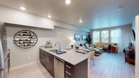 This single-floor residence offers a thoughtfully designed open-concept layout that seamlessly connects the kitchen, dining, and living areas. The kitchen serves as the heart of the home, anchored by a granite-topped island with an undermount sink, stainless steel appliances including a refrigerator, range, and microwave, and rich dark cabinetry accented by a decorative circular wine rack. Light wood-style flooring flows throughout the main living area, enhancing the bright and airy atmosphere.

The living room is generously proportioned, with large windows dressed in sheer curtains and blinds that invite abundant natural light and offer pleasant outdoor views. Neutral wall tones provide a calming backdrop throughout the space.

Two bedrooms offer comfortable retreats, each featuring plush carpeting, large windows, and ample closet space with sliding panel doors. The full bathroom is finished with a granite vanity countertop, an undermount sink, and a shower-tub combination.

A dedicated in-unit laundry area houses a full-sized washer and dryer side by side, with wire shelving above for additional storage. The overall design strikes a balance between modern functionality and understated warmth, making this a practical and inviting living space.