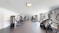 Located at 127 N 17th St in Richmond, VA, this fitness center offers a generously sized, single-floor layout designed to accommodate a comprehensive range of exercise needs. The space is organized with a clear, open floor plan finished with durable rubber flooring throughout, providing both functionality and safety for high-traffic use.

The cardio section is well-stocked with treadmills, stationary bikes, stair climbers, and elliptical machines, all positioned to take advantage of the abundant natural light streaming through large floor-to-ceiling windows along one side of the room. These windows also frame views of an adjacent outdoor pool and lounge deck, accessible directly through glass doors — a seamless indoor-outdoor connection.

On the strength training side, the facility features a variety of cable and selectorized machines, a dedicated free weights area with a dumbbell rack, adjustable benches, and functional training equipment including stability balls. The clean white walls and recessed flush-mount lighting contribute to a bright, modern aesthetic that keeps the space feeling open and energizing.

Additional amenities visible within the facility include an in-unit laundry area with washers and dryers enclosed behind glass-paneled doors, adding convenience for users. The overall design is modern and minimal, creating a professional gym environment well-suited for daily fitness routines.