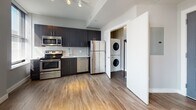 Located at 23 Central in Lynn, Massachusetts, this single-floor unit offers a well-designed, modern living space with a clean, contemporary aesthetic. The open-concept living and kitchen area is anchored by warm wood-look flooring that extends throughout the unit, complemented by neutral gray walls and crisp white trim. A bank of large windows lines the living area, allowing abundant natural light to fill the space and creating an airy, welcoming atmosphere. Track lighting overhead provides additional illumination throughout.

The kitchen is thoughtfully appointed with dark espresso cabinetry, a subway tile backsplash, and a full suite of stainless steel appliances, including a refrigerator, range, microwave, and dishwasher. A dedicated in-unit laundry closet with a stacked washer and dryer is conveniently located just off the kitchen.

The bedroom features a double-door closet offering generous storage, while the surrounding neutral-toned walls and consistent flooring maintain the unit's cohesive modern design. An additional versatile room provides flexible living space. The bathroom is finished with large-format tile flooring, a full tub-shower combination, and a white vanity with ample counter space, rounding out this well-appointed home.