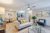This single-story residence offers a thoughtfully designed open-concept layout that seamlessly connects the living, dining, and kitchen areas. The living room is a welcoming focal point, featuring light wood-style flooring, a ceiling fan with integrated lighting, and a classic fireplace with a white mantel flanked by windows dressed with blinds and patterned curtains. A glass-top coffee table and neutral-toned sofa with bold accent pillows complete the space.

The galley-style kitchen is well-equipped with dark cabinetry, granite-look countertops, stainless steel appliances including a refrigerator, microwave, and dishwasher, as well as a breakfast bar with seating. The kitchen connects directly to an in-unit laundry room housing a full-size washer and dryer.

The bedroom provides a serene retreat with plush carpeting, a natural light-filled window with decorative curtains, and access to a generously sized walk-in closet outfitted with wire shelving and hanging rods. The bathroom features a granite-top vanity with dark cabinetry, a framed mirror, and a shower/tub combination. Throughout the space, a warm, neutral color palette and consistent finishes create a cohesive and inviting ambiance.