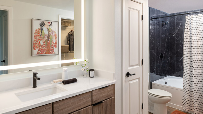 Apartment bathroom with large soaking tub, wood-style flooring and LED vanity mirror. - Griffis at The Domain