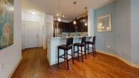 Located at City Walk Way in Charlottesville, Virginia, this single-floor residence offers a thoughtfully designed layout with cohesive finishes throughout. The kitchen is a standout feature, equipped with dark espresso cabinetry, granite-style countertops, and a full suite of stainless steel appliances including a refrigerator, range, and built-in microwave. A peninsula with pendant lighting and bar-height seating provides both additional prep space and a casual dining area, while warm hardwood-style flooring ties the kitchen seamlessly to the adjoining living area.

The living room is accented by a soothing teal-blue feature wall, complemented by hardwood-style flooring and an open connection to the kitchen. Multiple bedrooms offer plush carpeting, natural light through large windows, and ample space for furnishings. Each bedroom carries a distinct character, with one featuring a bold teal accent wall and another finished in soft, neutral tones.

The bathrooms are finished with large-format tile flooring, dark vanity cabinetry, and granite-style countertops. One bathroom includes a walk-in closet directly accessible from the space, adding practical storage. Overall, the residence presents a modern, comfortable aesthetic with consistent quality finishes throughout.