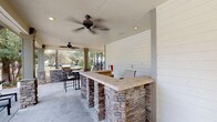 This outdoor amenity space is thoughtfully designed to provide a comprehensive recreational experience. At the heart of the area is a generously sized, covered pavilion featuring a built-in bar constructed with stacked stone bases and a tiled countertop, ideal for outdoor entertaining. Ceiling fans are mounted overhead to ensure comfort during warm weather, while recessed lighting and shiplap-accented walls add a polished, finished aesthetic to the covered area. Additional built-in grilling and prep stations extend the outdoor kitchen functionality.

The centerpiece of the complex is a resort-style swimming pool with a curved, free-form design framed by a broad brick-paved deck. Cushioned lounge chairs are positioned poolside, offering ample space for relaxation. Umbrella-shaded tables and seating clusters provide comfortable gathering spots throughout the deck area.

The surrounding courtyard is finished with decorative brick pavers and is framed by mature trees and well-maintained landscaping beds. The multi-story brick exterior buildings, featuring bay windows, balconies, and pitched rooflines, create an attractive and cohesive architectural backdrop. Walkways meander through the greenery, connecting all areas of the community with a welcoming, park-like atmosphere.