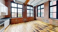 Located at 95 Chestnut St in Providence, Rhode Island, this loft-style unit showcases the character of a thoughtfully converted industrial building. The open-plan living area is defined by striking exposed brick walls, original hardwood floors with rich tonal variation, and soaring ceilings that lend an expansive, airy feel. Oversized, black-framed industrial windows line the walls, inviting abundant natural light and offering views of the surrounding Providence streetscape. Exposed ductwork and wooden ceiling beams add to the authentic industrial aesthetic throughout.

The kitchen is efficiently designed and well-appointed, featuring white shaker-style cabinetry, dark countertops, and a full suite of stainless steel appliances — including a refrigerator, electric range, and dishwasher — all set against the backdrop of the unit's signature brick walls and hardwood floors.

The bathroom is clean and modern, finished with white subway tile in the walk-in shower, light tile flooring, white cabinetry with stone-topped vanity, and contemporary chrome fixtures. The overall ambiance of this space blends historic industrial charm with practical modern updates, making it a distinctive offering in the heart of Providence.