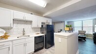 Located at 722 Walnut St in Kansas City, MO, this one-bedroom unit offers a thoughtfully arranged single-floor layout comprising a living room, kitchen, bedroom, and hallway. The kitchen is a standout feature, outfitted with crisp white shaker cabinetry, a subway tile backsplash, white countertops, and black appliances including a range, microwave, dishwasher, and refrigerator. A peninsula counter provides additional workspace and a natural transition into the living area. The living room is bright and welcoming, benefiting from large windows with horizontal blinds that allow ample natural light to fill the space. Hardwood-style flooring runs consistently throughout, lending a clean, cohesive aesthetic. Neutral-toned walls create a calm, versatile backdrop across all rooms. The bedroom is a comfortably sized private retreat, featuring a double-door closet for generous storage, a window for natural light, and continued hardwood-style flooring. A connecting hallway links the rooms efficiently, with additional storage access. Textured ceilings are present throughout. The overall ambiance is modern, clean, and functional, offering a practical yet comfortable living environment in the heart of Kansas City.