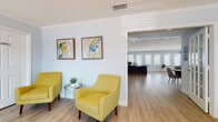 Located at 3132 W Lambright St in Leto, FL, this single-floor professional office space offers a thoughtfully designed layout ideal for a client-facing business. The entry reception area sets a welcoming tone with light blue-gray walls, light wood-look flooring, crown molding, and vibrant yellow accent chairs paired with framed abstract artwork. A seamless flow connects the reception to a central dining or conference nook, featuring a round wood table with seating for four, contemporary abstract wall art, and convenient access to multiple areas of the suite via a classic French door. The primary private office is generously proportioned, bathed in natural light through a bank of white-shuttered windows along one wall, and includes a dedicated workspace desk alongside a comfortable seating area — ideal for client consultations. An additional flexible area provides space for relaxing or informal meetings, accented with tasteful wall décor and area rugs. The kitchenette is equipped with stainless steel appliances including a refrigerator and microwave, white cabinetry, a granite-style countertop, and a pass-through bar with bar stools. Throughout, the cohesive soft color palette, consistent flooring, and clean architectural lines create a calm, professional ambiance well-suited for a variety of office or wellness-oriented uses.