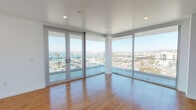 Located in San Diego's vibrant Little Italy neighborhood, this modern residence at 915 W Grape St offers a thoughtfully designed single-floor layout with a clean, contemporary aesthetic throughout. The standout feature of the living area is the dramatic wraparound floor-to-ceiling windows and glass doors that flood the space with natural light and frame sweeping panoramic views of the marina, harbor, and palm-lined surroundings — creating an open, airy atmosphere that seamlessly connects the interior to the coastal scenery beyond.

Warm-toned hardwood flooring runs consistently throughout the space, lending a cohesive and inviting feel to every room. The modern kitchen is equipped with stainless steel appliances, including a range, microwave, and dishwasher, complemented by sleek white cabinetry, light countertops, and a white subway tile backsplash. The layout flows naturally through a well-lit hallway connecting the private rooms and bathrooms. Bedrooms are bright and clean, with recessed lighting and large windows offering additional harbor-facing views. The bathrooms feature white subway tile, modern vanities, and both a walk-in shower and a separate soaking tub option, maintaining the home's crisp, minimalist design throughout.